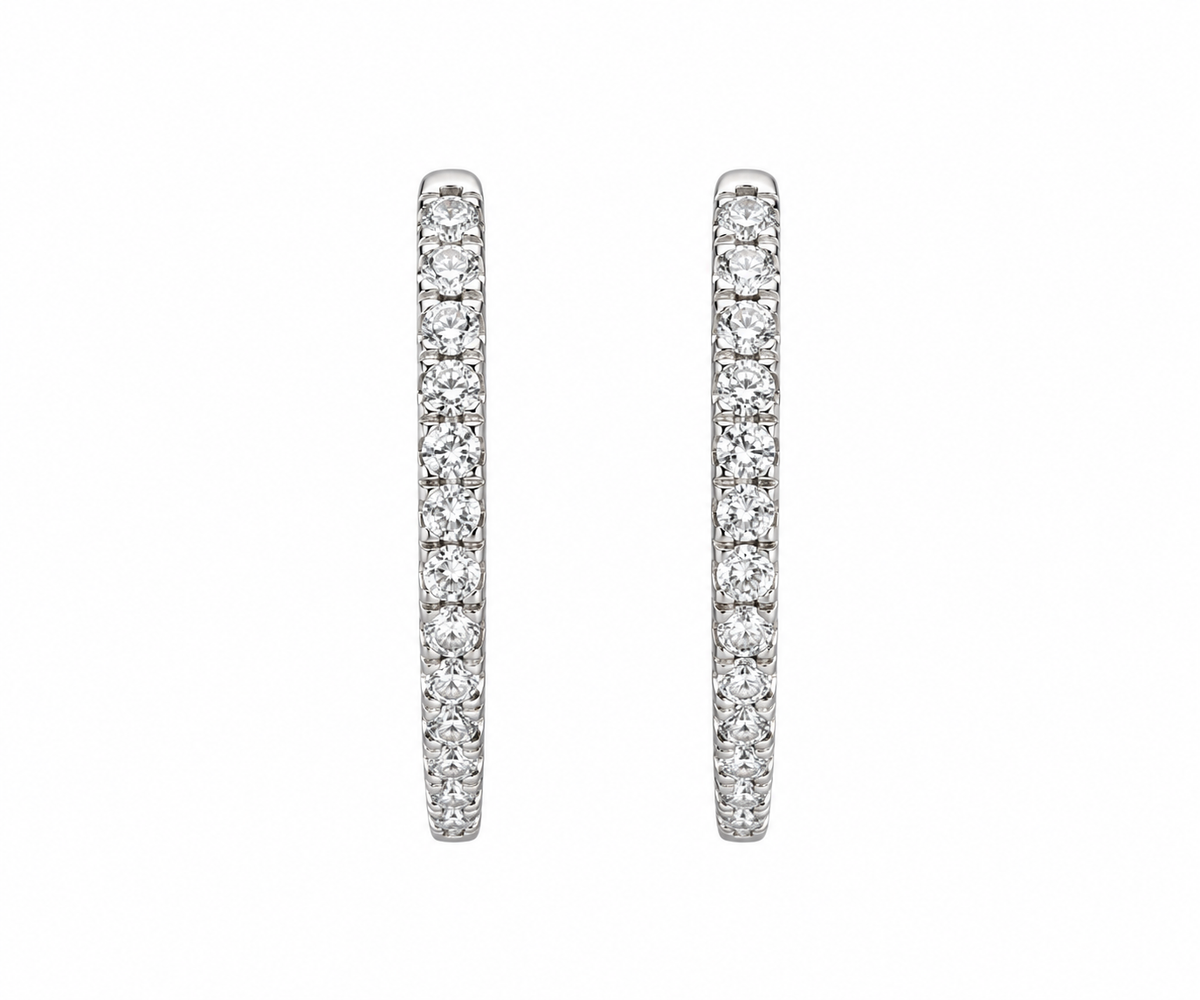 A pair of silver-toned huggie hoop earrings paved with round clear stones, shown against a plain white background.