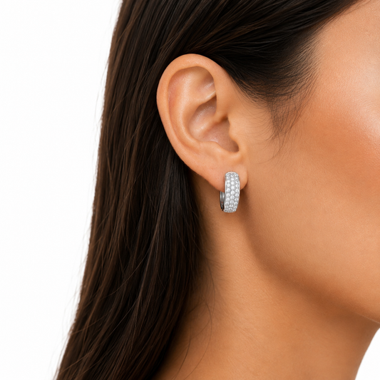 A close-up side view of a woman's ear wearing a small silver hoop earring set with clear stones, against a clean white background.