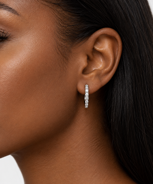 A close-up side profile of a woman wearing a single silver-toned vertical pavé dangle earring with clear stones.